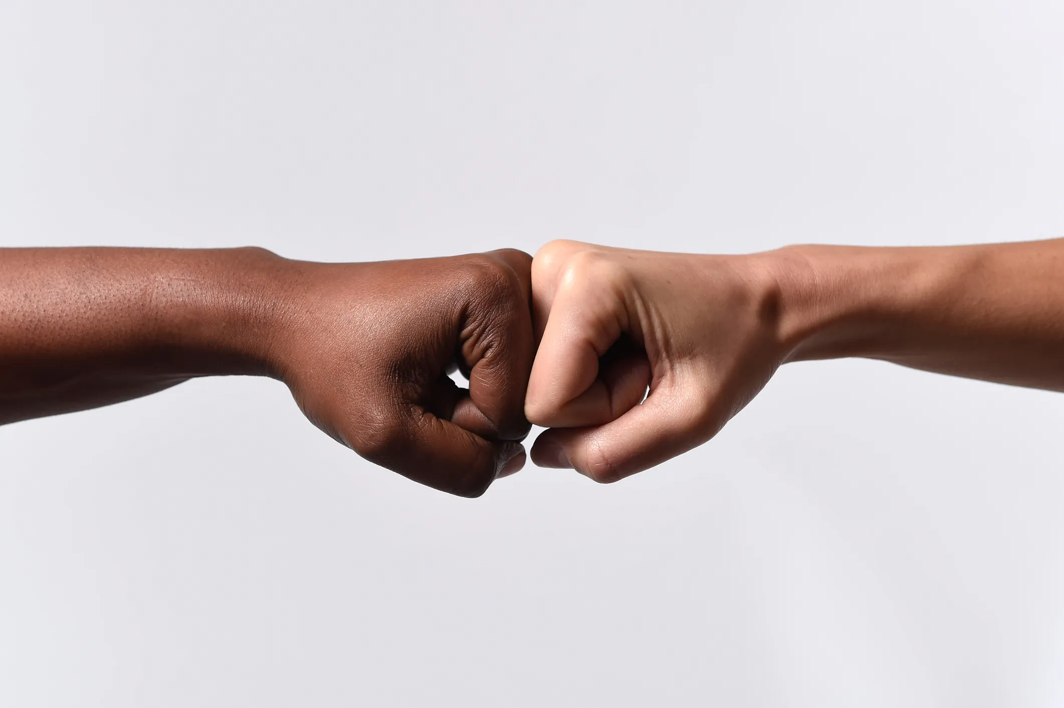 Close-up image of a Black person and a White person touching knuckles in a fist bump gesture, symbolizing unity, friendship and racial harmony in the context of discussing interracial attitudes and perceptions